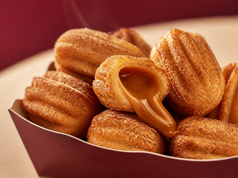 Mini churros dourados com doce de leite cremoso aparecendo