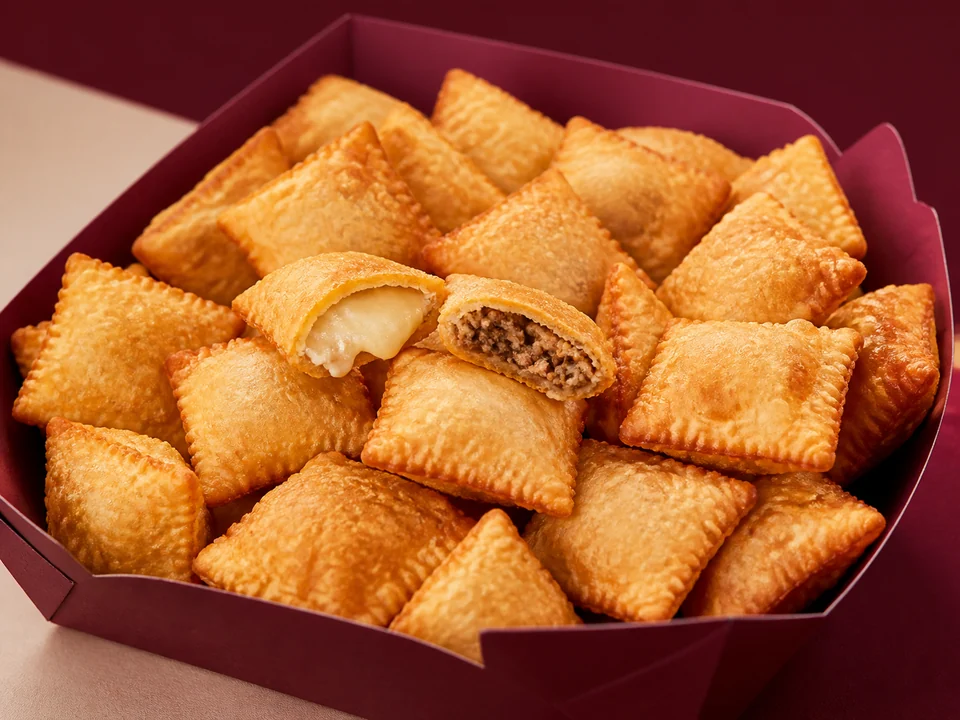 Mini pastéis quadradinhos e dourados, com queijo e carne aparecendo por dentro